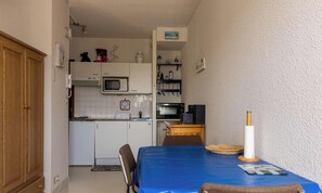 A compact kitchen with a microwave, stove, and a small refrigerator. There is a dining table with a blue tablecloth and a candle holder. - 2-person apartment near the beach in Sables-d’Or-les-Pins | Ref 115 (SABLES D OR LES PINS)