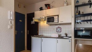 Pieni, käytännöllinen keittiö, jossa on valkoiset kaapit, mikroaaltouuni, liesi ja pesuallas.