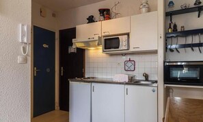A compact kitchen with white cabinets, a microwave, a stove, and a sink. - 2-person apartment near the beach in Sables-d’Or-les-Pins | Ref 115 (SABLES D OR LES PINS)