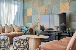 A modern living room with a sofa, ottoman, and coffee table, a flat-screen TV mounted on a stone wall, and a cactus on a side table. - Terrace Living and Views in Iconic Roma Norte (Mexico City)