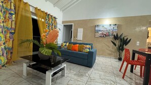 Un salón con un sofá azul, cojines anaranjados, una mesa de centro negra y una planta en maceta.
