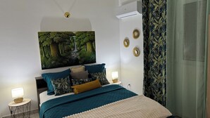 Un dormitorio con cama, mesita de noche, aire acondicionado de pared y un cuadro con paisaje de bosque.