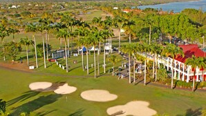 Un campo de golf con búnkeres de arena, palmeras y un edificio de techo rojo.