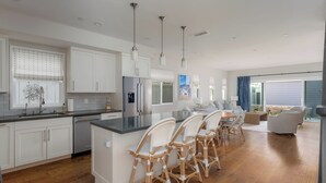 Een moderne keuken met witte kasten, een centraal eiland met barkrukken en een eethoek met een groot raam.