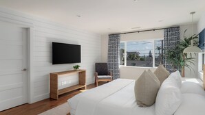 Een moderne slaapkamer met een groot bed, een aan de muur bevestigde televisie, een houten console tafel, een stoel en een raam met behang.