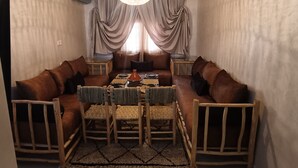 Een gezellige woonkamer met een bruine zithoek, een geweven salontafel en een kroonluchter.