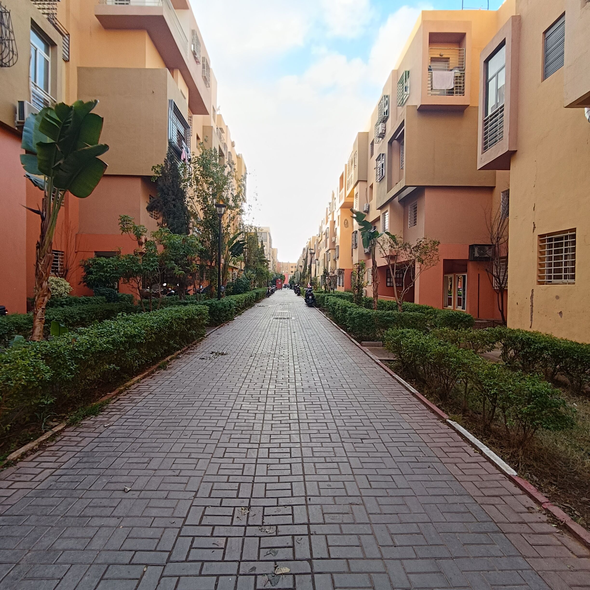 Un chemin pavé bordé de bâtiments dotés de balcons et de fenêtres, qui mène à un quartier résidentiel.