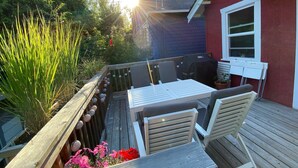 Una terraza de madera con una mesa y sillas, rodeada de macetas con plantas y una valla de madera.