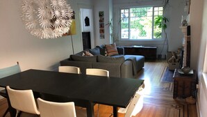 Una sala de estar moderna con comedor, un conjunto de sofás, un ventanal grande y una lámpara decorativa.