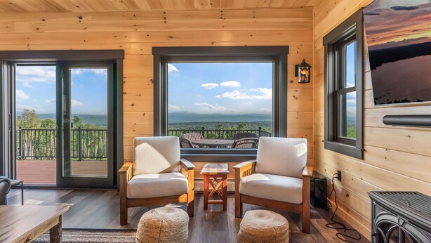 Een houten chalet met een balkon, twee stoelen, een kleine tafel en een open haard.