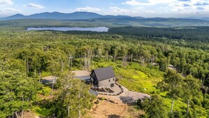 Een huis omgeven door dicht bos, met een meer en bergen op de achtergrond.