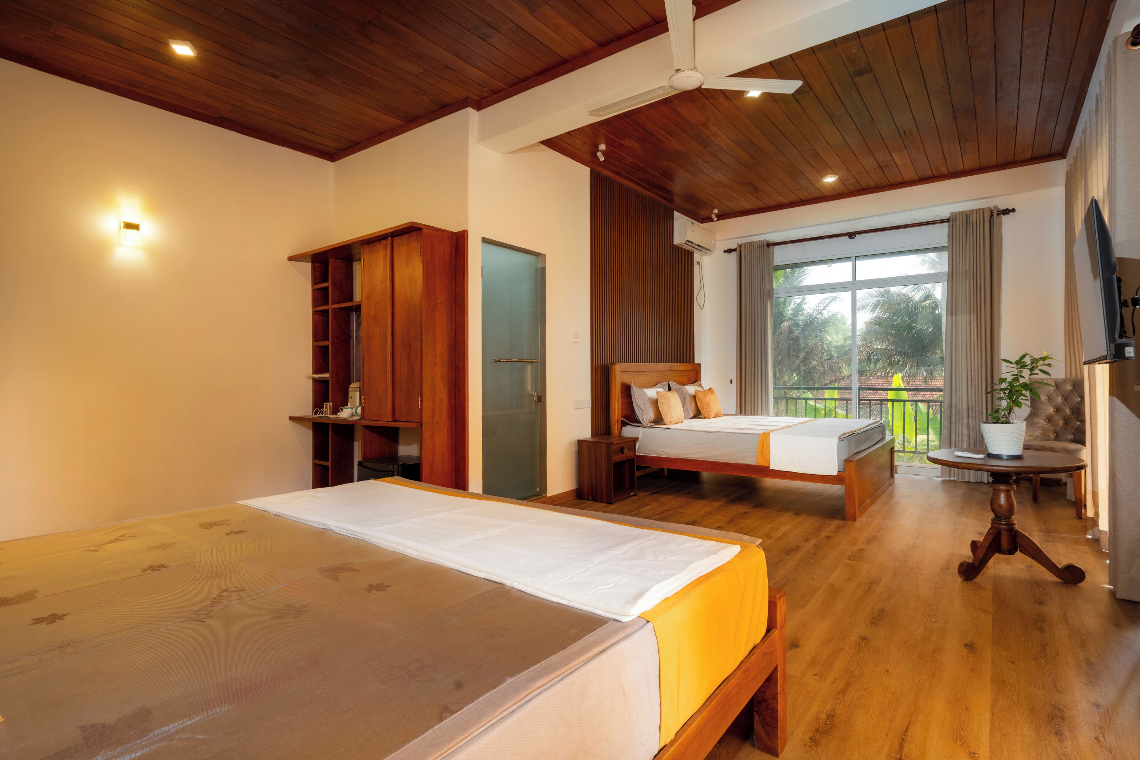 A bedroom with a large bed, a smaller bed, a wardrobe, a ceiling fan, and a balcony with a view.