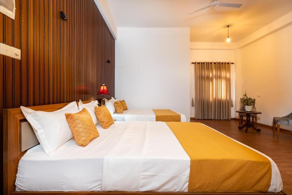 A hotel room with two beds, wooden paneling on one wall, a ceiling fan, and a window with curtains.
