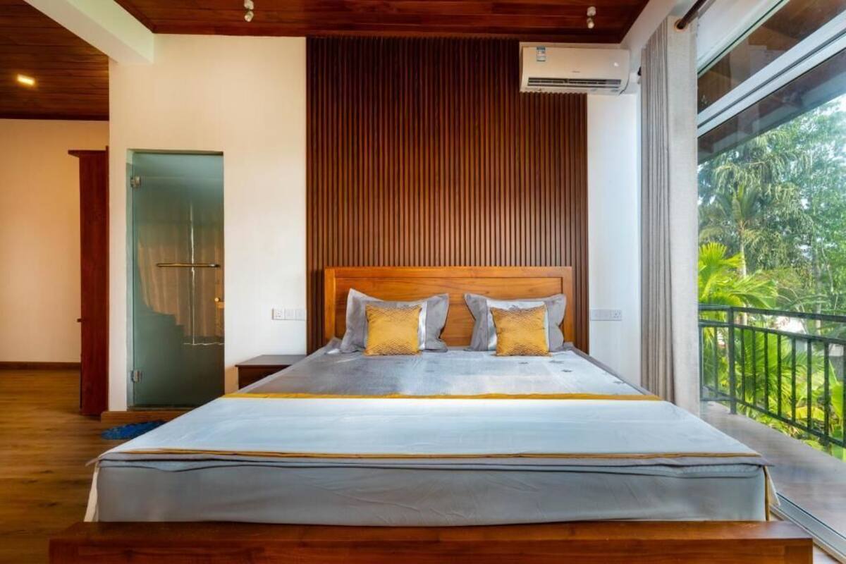 Une chambre dotée d’un grand lit, d’une tête de lit en bois et d’un balcon offrant une vue sur la verdure.