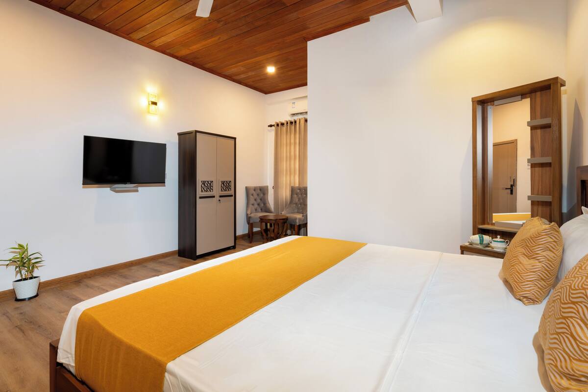 Une chambre d’hôtel comprenant un lit, un téléviseur fixé au mur, une armoire, un bureau avec une lampe et une plante en pot.