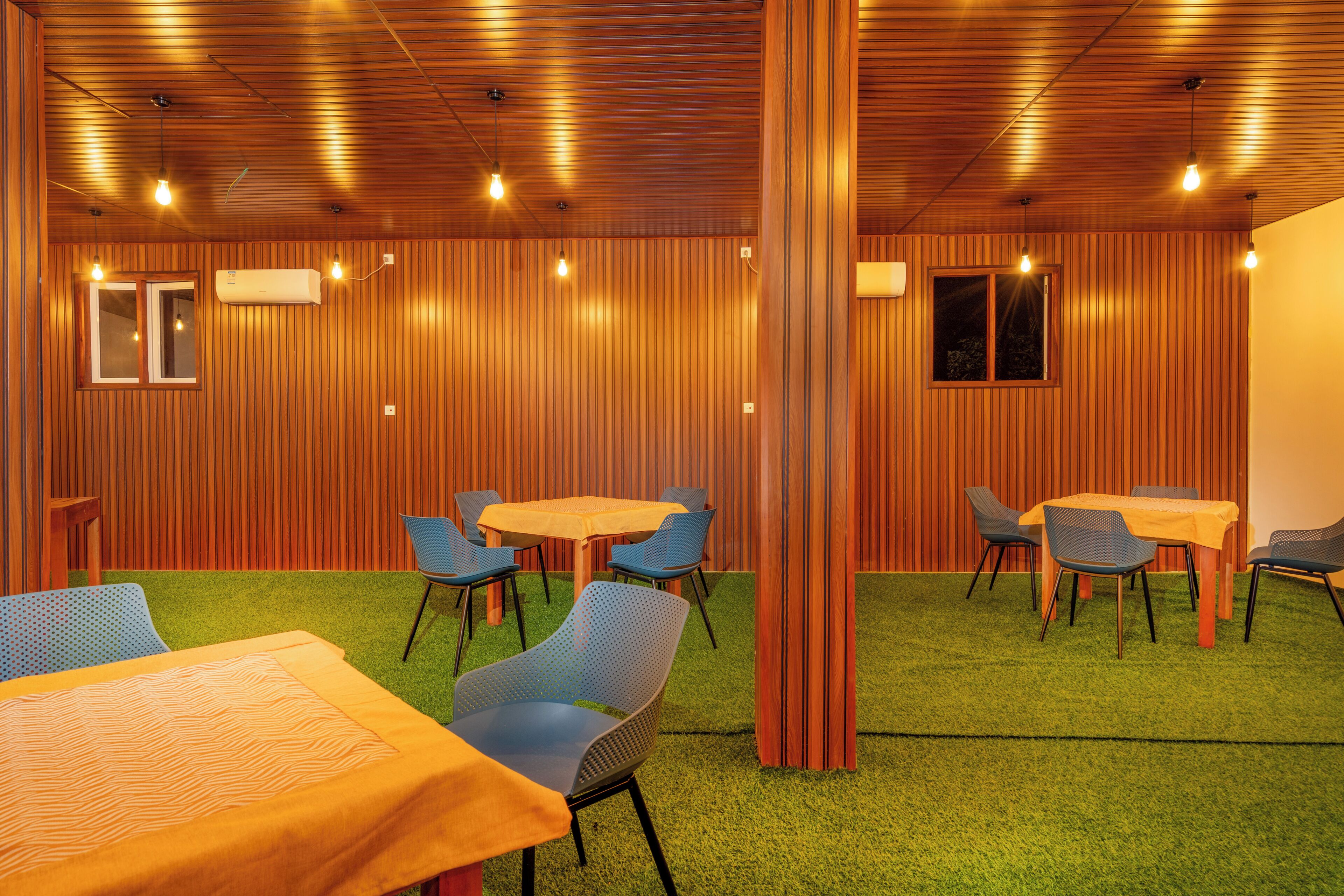 Una habitación con paredes de madera, alfombra verde y varias mesas y sillas.