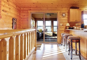L’intérieur d’un chalet en bois, avec un balcon, un coin cuisine et un salon comprenant un canapé et une fenêtre.