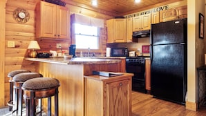 A wooden cabin kitchen with a black refrigerator, wooden cabinets, a bar stool area, and a 'Live Laugh Love' sign.