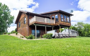 A two-story wooden house with a balcony, large windows, and a satellite dish.