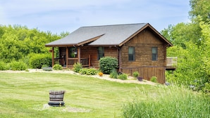 A wooden cabin with a porch, surrounded by a well-maintained lawn and various plants.