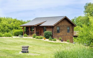 A wooden cabin with a porch, surrounded by a well-maintained lawn and various plants.