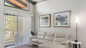 Una sala de estar con un sofá seccional color crema, un tapiz estampado, dos cuadros enmarcados, una lámpara de pie y vistas a través de una puerta corrediza.