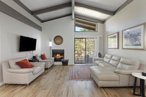 A living room with a fireplace, sofas, a TV, and artwork on the walls. - 2BR Sedona condo with pool, hot tub, fireplace, balcony and garden views. (Sedona)