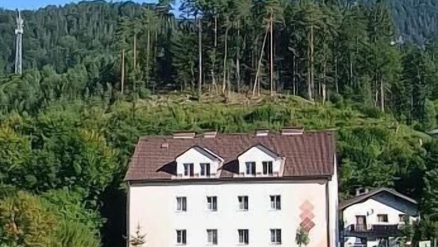 Un edificio de dos plantas con fachada simétrica, rodeado de un césped cuidado y un bosque denso al fondo.