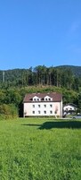 Un edificio de dos plantas con fachada simétrica, rodeado de un césped cuidado y un bosque denso al fondo.