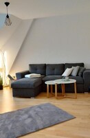 Una sala de estar moderna con un sofá modular gris oscuro, una mesa de centro redonda de madera y una alfombra gris sobre piso de madera.