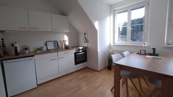 Una cocina moderna con armarios blancos, horno integrado y comedor con mesa y sillas de madera.