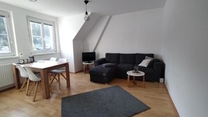 Una sala moderna con una mesa de comedor de madera, sillas blancas, un sofá oscuro y una pequeña mesita auxiliar.