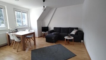 Una sala moderna con una mesa de comedor de madera, sillas blancas, un sofá oscuro y una pequeña mesita auxiliar.