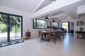 Une cuisine spacieuse avec de grandes fenêtres, un coin repas avec une table et des chaises en bois, et une vue sur la verdure à l’extérieur.