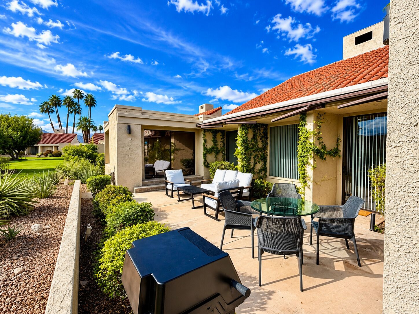A patio with outdoor furniture, a barbecue grill, and a view of a residential area with palm trees.