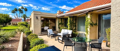 A patio with outdoor furniture, a barbecue grill, and a view of a residential area with palm trees.