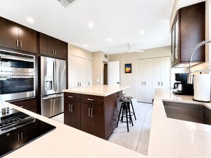 A modern kitchen with stainless steel appliances, a central island, and bar stools. - Grande Vista Villa: 3 bed/3 bath Luxury Living; Stunning Lake & Mountain Views | a Greenday property (Rancho Mirage)