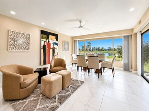 A modern living room with a dining area, large windows, and artwork on the walls. - Grande Vista Villa: 3 bed/3 bath Luxury Living; Stunning Lake & Mountain Views | a Greenday property (Rancho Mirage)