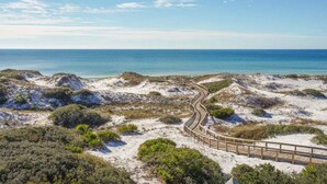 Ein Sandstrand mit einem hölzernen Promenadenweg, der sich durch Dünen schlängelt und zum Meer führt.