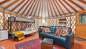 Interior acogedor de una yurtas con una litera, un sofá de cuero azul y una alfombra estampada.