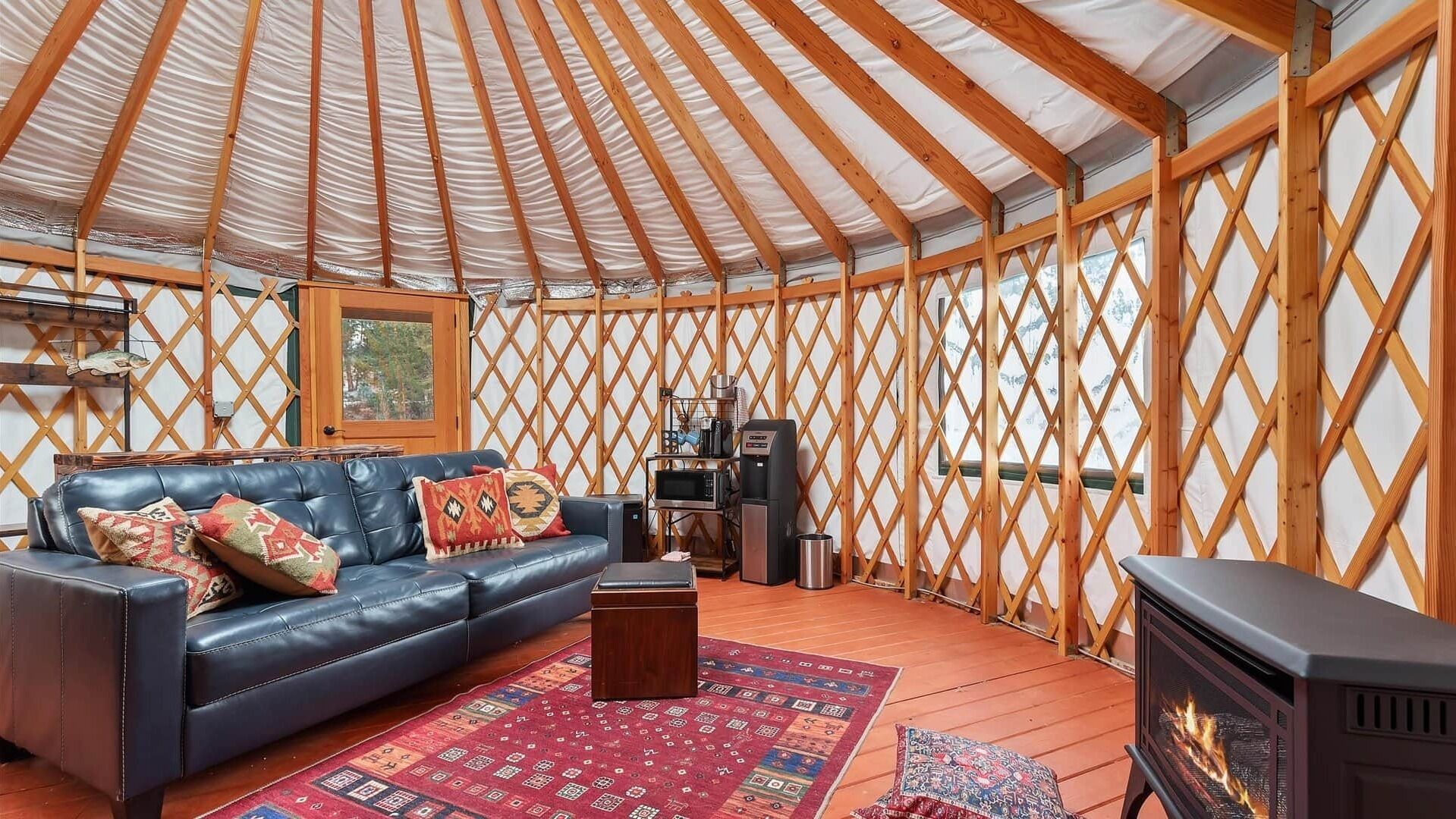 A yurt interior with a leather sofa, a rug, a coffee machine, and a wood stove.