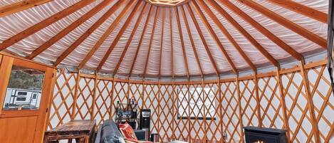 A yurt with a wooden lattice wall, a black sofa, a small table, and a wood-burning stove.