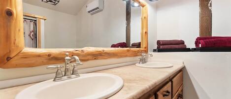 A bathroom with two sinks, wooden vanity, a large mirror, and a towel rack with towels.