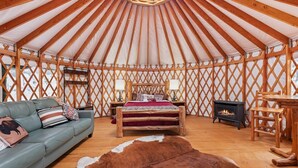 A yurt with a wooden interior, a bed with a red blanket, a sofa, a small table, and a fireplace. - Yurt 2 - The Gold Miner (Boise County)