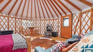 A yurt interior with a wooden lattice wall, a central table, chairs, a bed, and a small kitchenette. - Yurt 2 - The Gold Miner (Boise County)