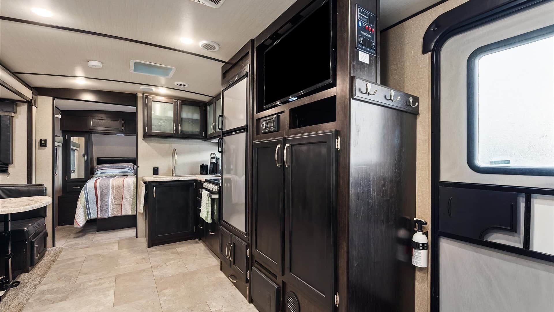 A compact RV interior with a kitchenette, a bed, and a small dining area.