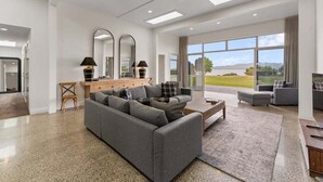 A modern living room with a grey sectional sofa, a wooden coffee table, and a large window offering a view of the outdoors. - Lakefront Kuiwai - lakefront with spa pool (Taupo)