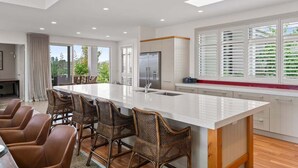 A modern kitchen with a large island, bar stools, and a view of greenery outside. - Lakefront Kuiwai - lakefront with spa pool (Taupo)