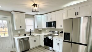 A modern kitchen with white cabinetry, stainless steel appliances, and a wooden floor. - Cozy 2-bedroom cottage (New Orleans)