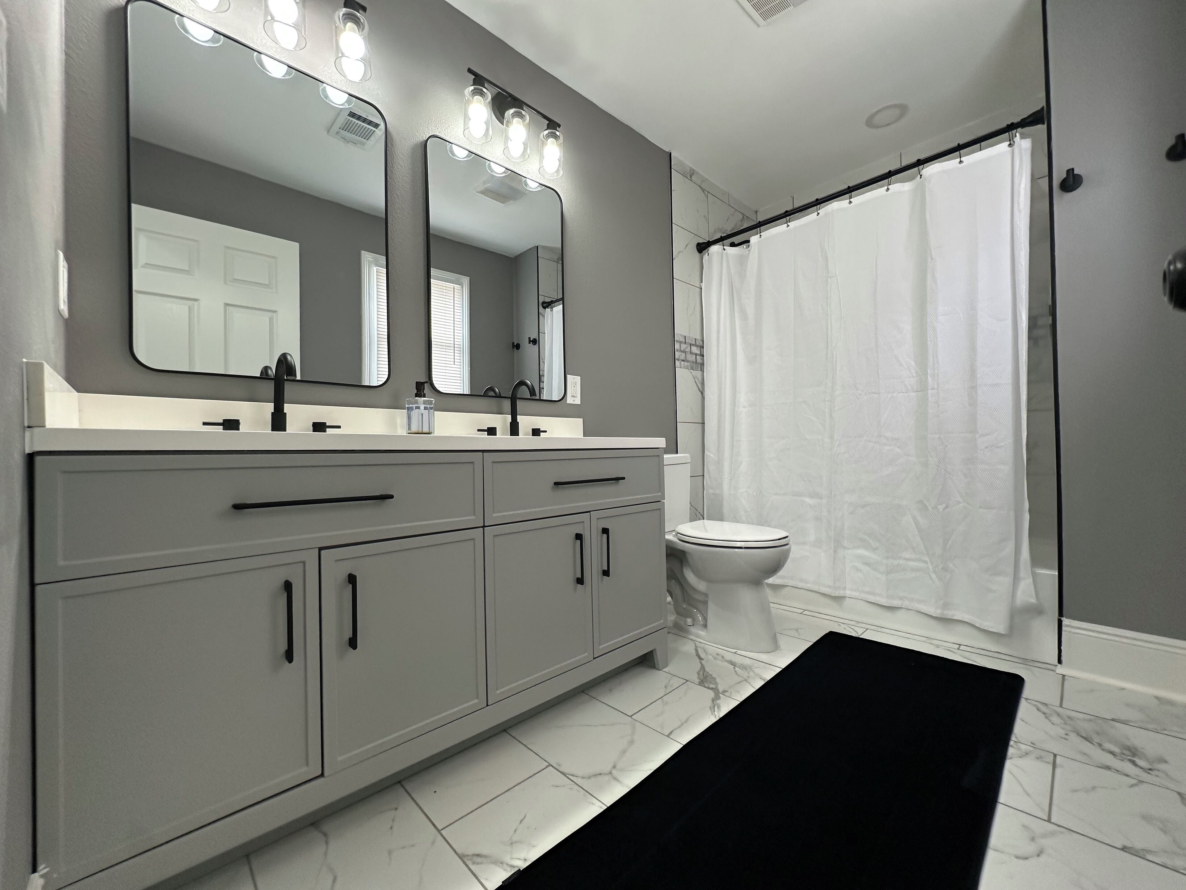 A modern bathroom with a grey vanity, a large mirror, a white toilet, and a shower curtain.